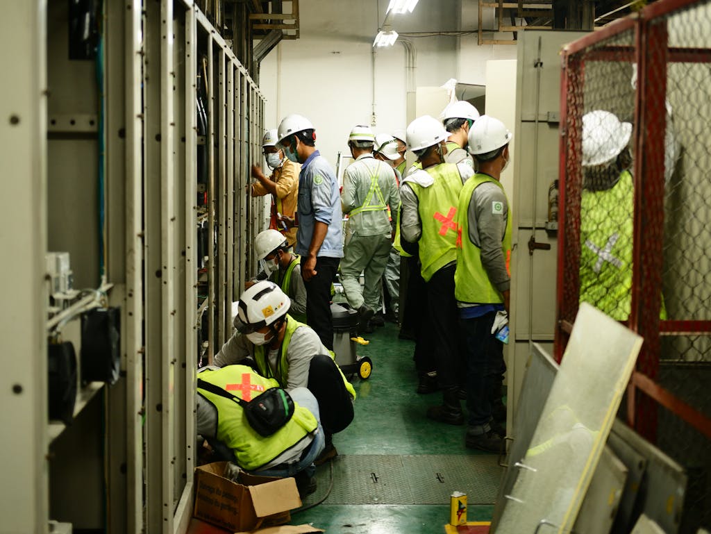Group of construction workers in an industrial room, wearing helmets and safety vests, working together.